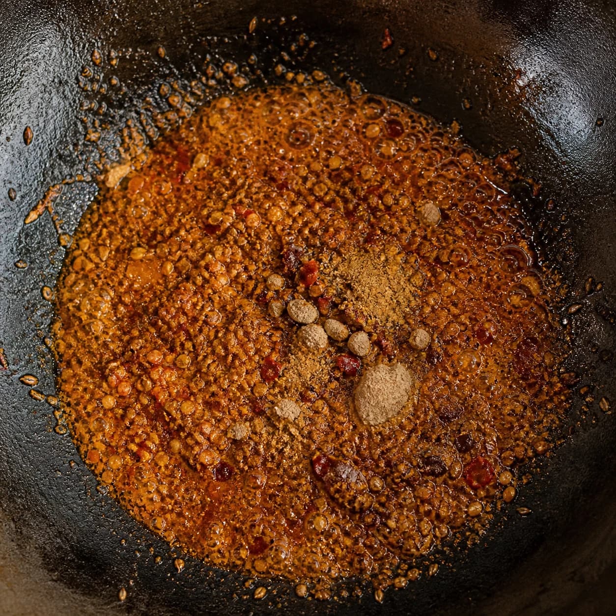 Cumin, ajwain and ground Pindi Cholley spices blooming briefly in hot ghee in a dark iron kadai