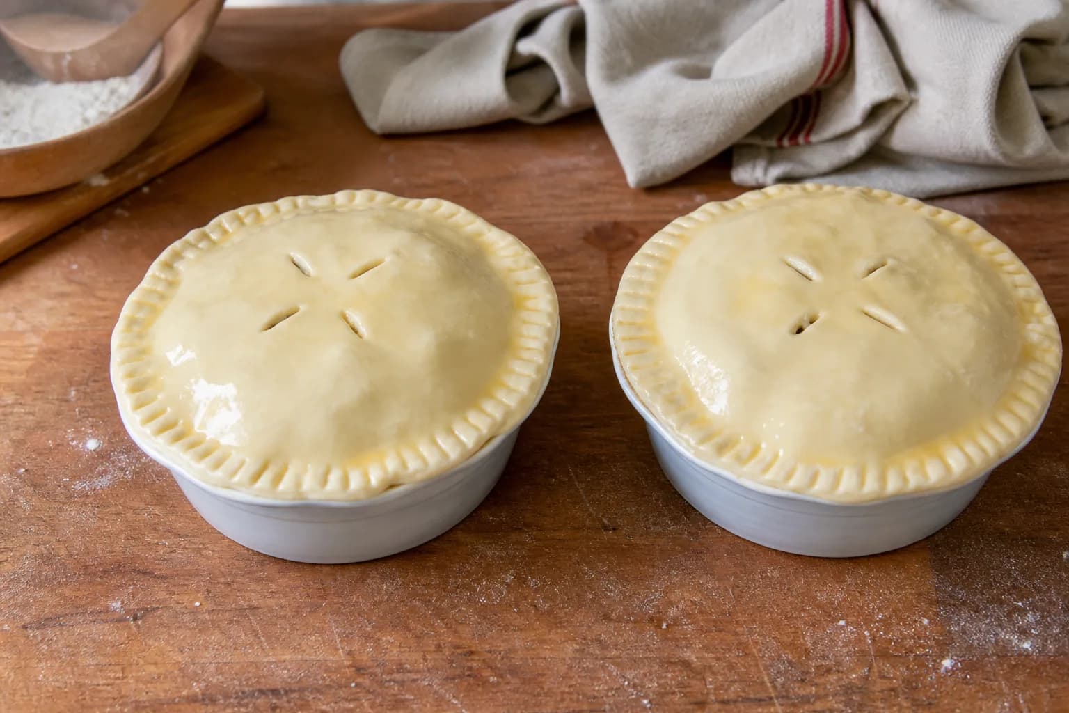 Two individual steak and ale pies with crimped unbaked pastry lids and four steam slits