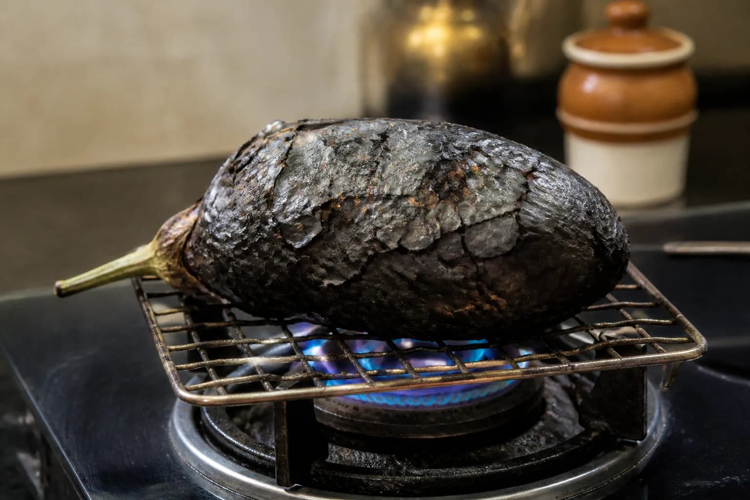 A whole aubergine with blackened blistered skin roasting over a gas flame